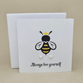 A pair of silver heart shaped earrings are displayed on a white gift card featuring a bee illustration and the phrase 'Always bee yourself'.