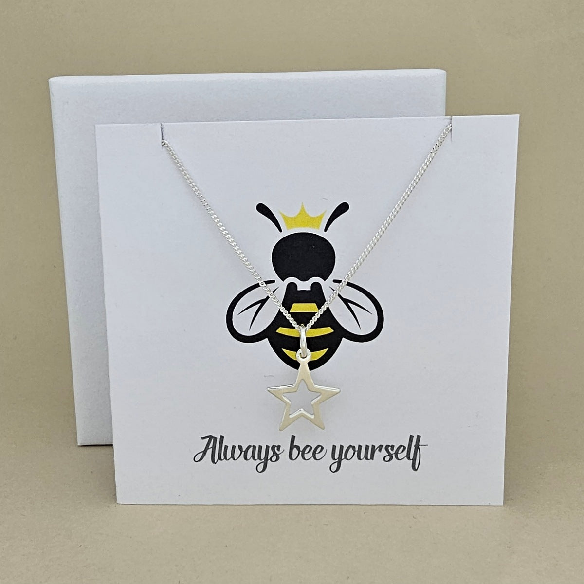 A silver necklace with an open star shaped pendant is displayed on a white gift card featuring a bee illustration and the phrase 'Always bee yourself'.