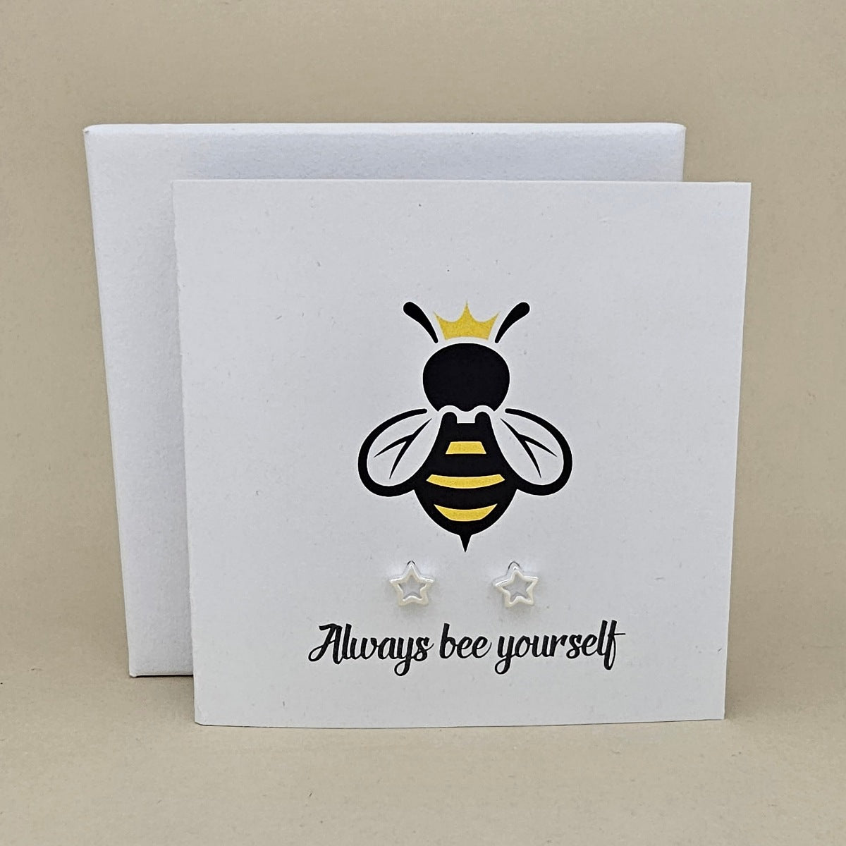 A pair of silver open star shaped earrings are displayed on a white gift card featuring a bee illustration and the phrase 'Always bee yourself'.
