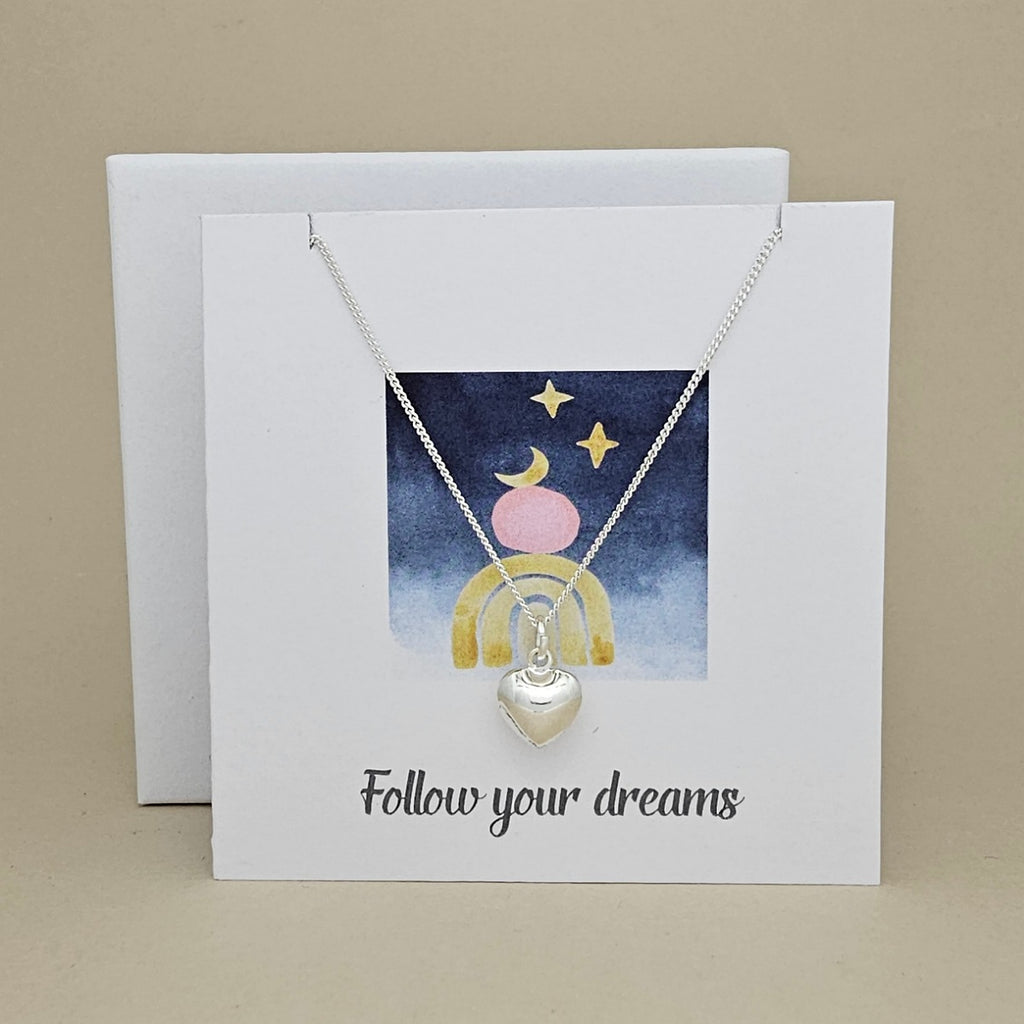 Silver necklace with heart pendant on a card with 'Follow your dreams' text and celestial design.