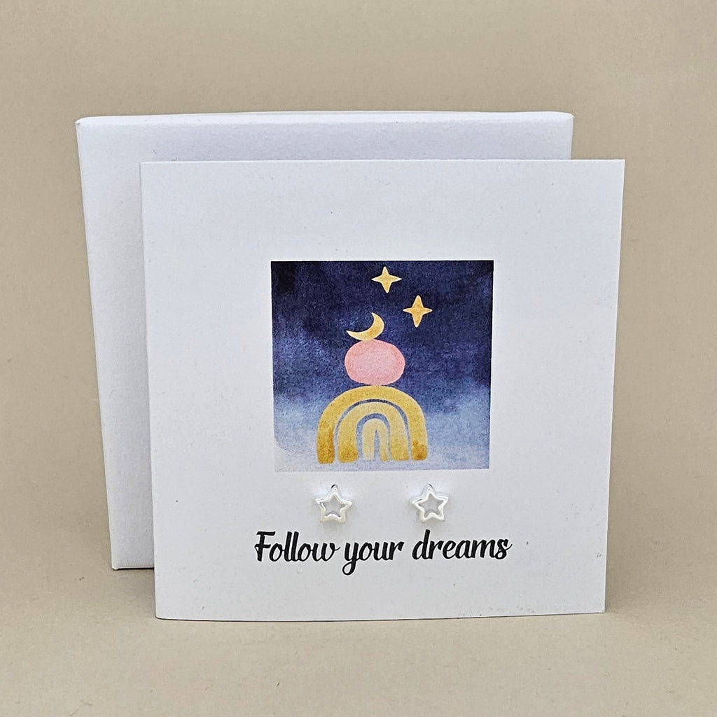 White card with a celestial design and a pair of silver open star earrings and 'Follow your dreams' text on a beige background