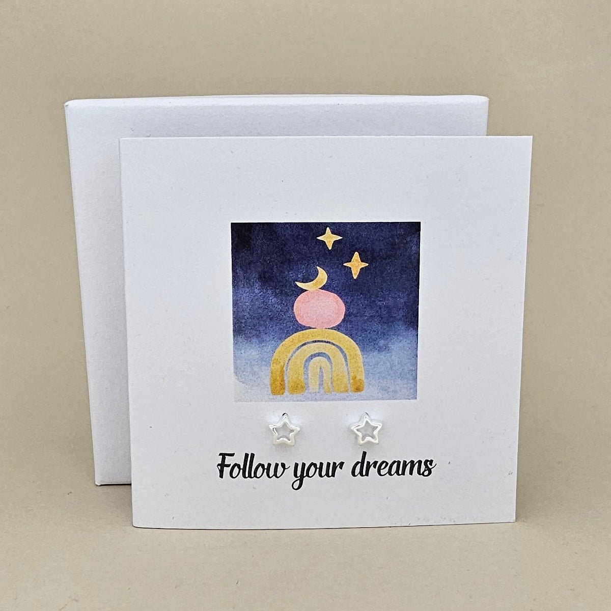 White card with a celestial design and a pair of silver open star earrings and 'Follow your dreams' text on a beige background
