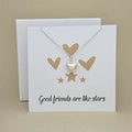 A silver heart pendant necklace on a delicate chain, displayed on a white card that reads 'Good friends are like stars' with gold heart and star graphics, set against a beige background.