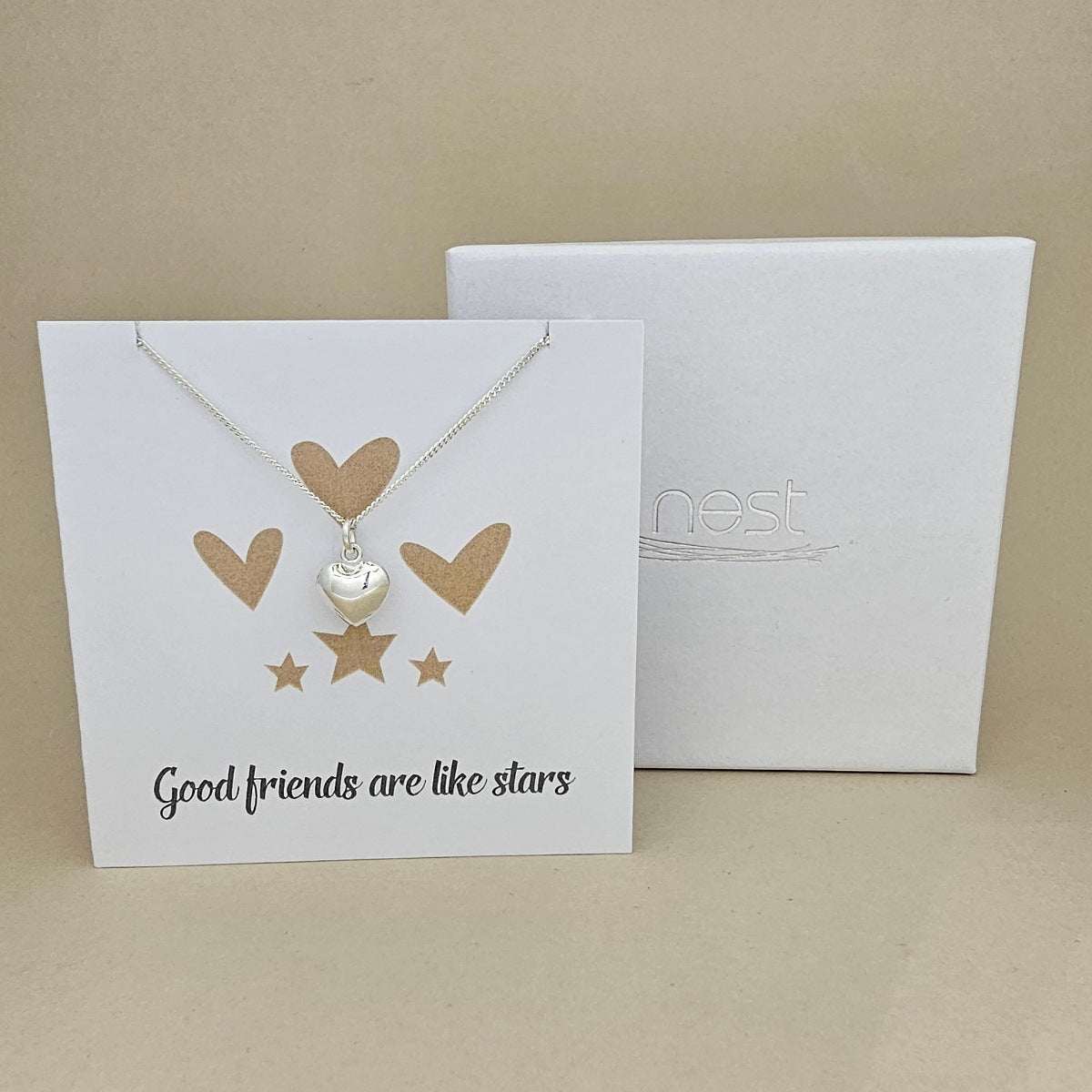 Silver necklace with heart and star pendant on a card with 'Good friends are like stars' text, next to a branded 'nest' box.