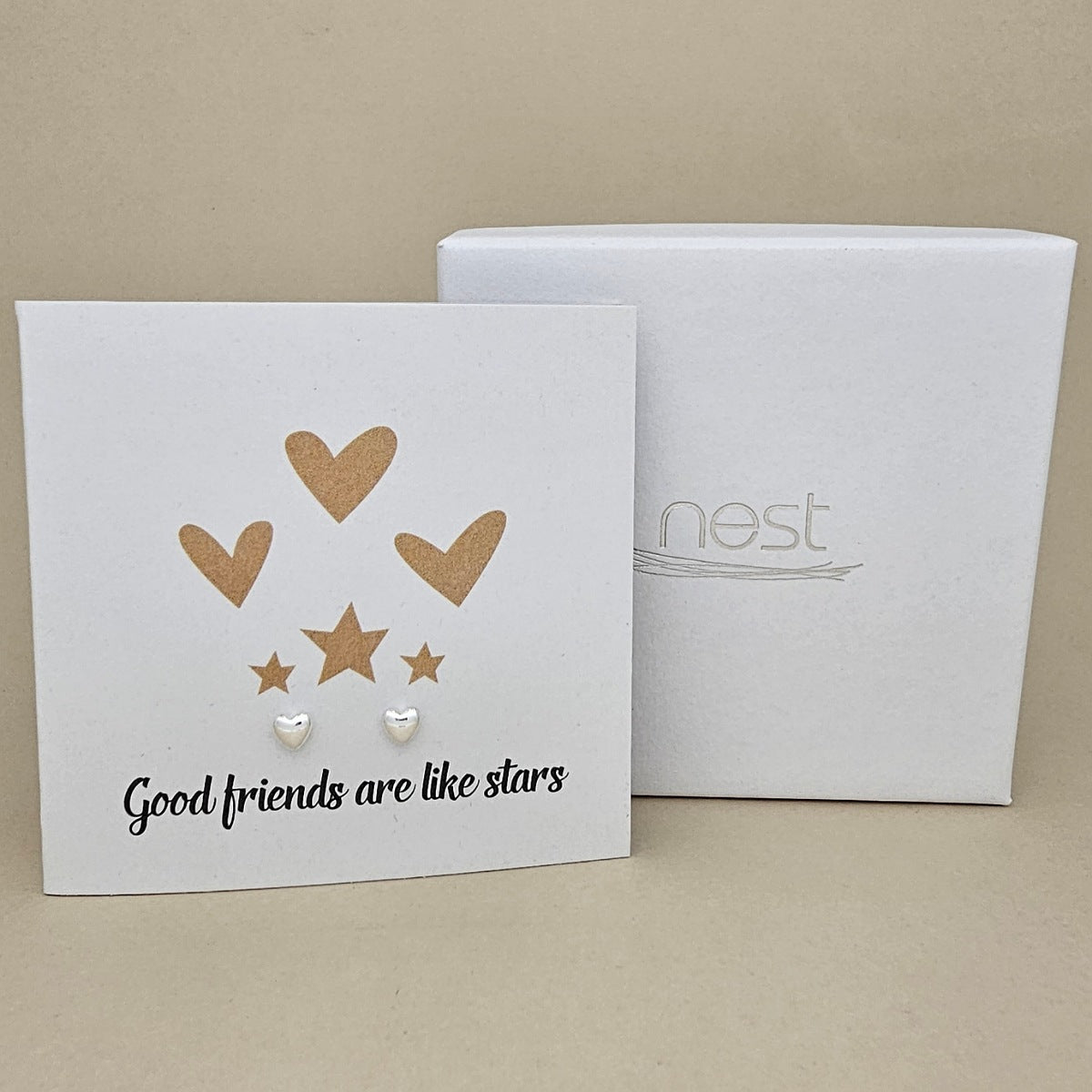 Card with a pair of silver heart earrings and gold heart and star designs and text 'Good friends are like stars' on a beige background