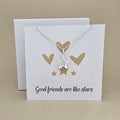 Silver necklace with open star pendant on a white card with gold heart and star illustrations and text 'Good friends are like stars'.