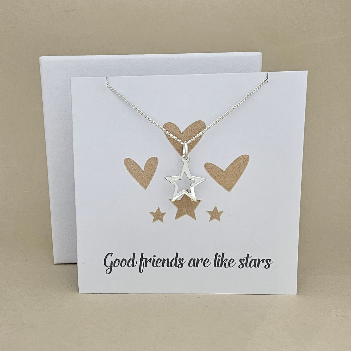 Silver necklace with open star pendant on a white card with gold heart and star illustrations and text 'Good friends are like stars'.