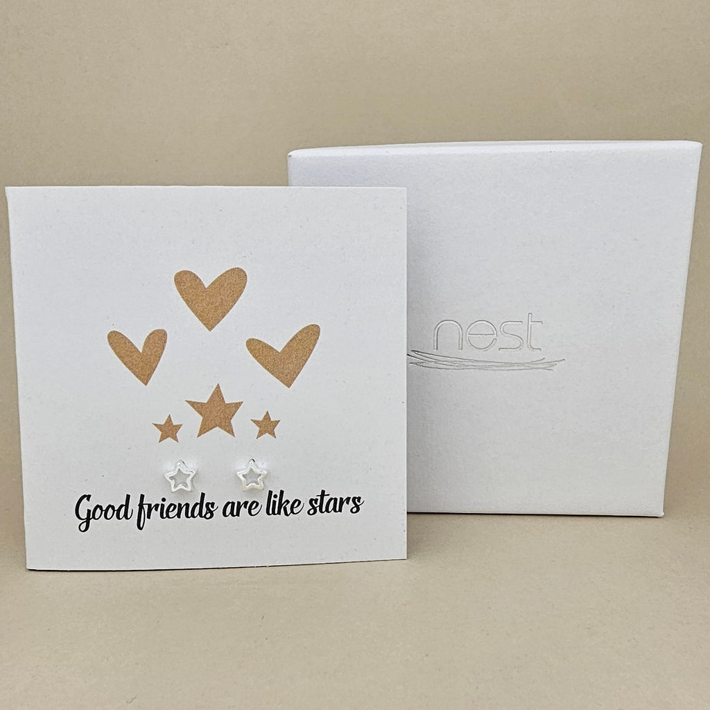Card with gold hearts and stars design and 'Good friends are like stars' text, pair of silver open star earrings next to a white box with 'nest' branding.