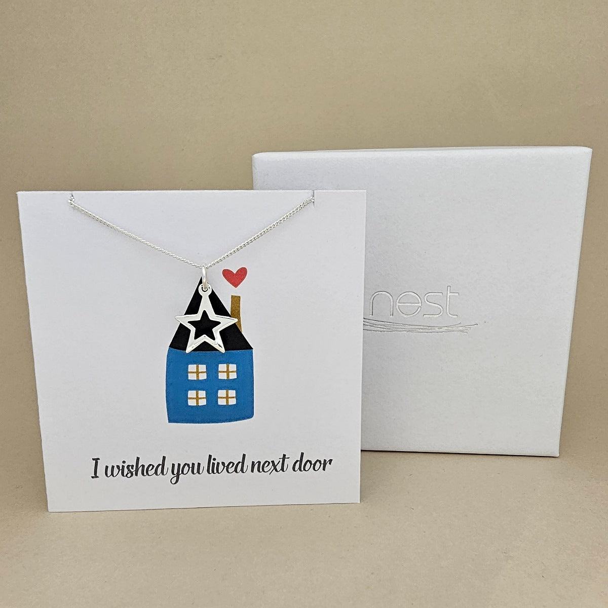 Necklace with star pendant on a card labelled 'I wished you lived next door' with an image of a house next to a branded 'Nest' white box.
