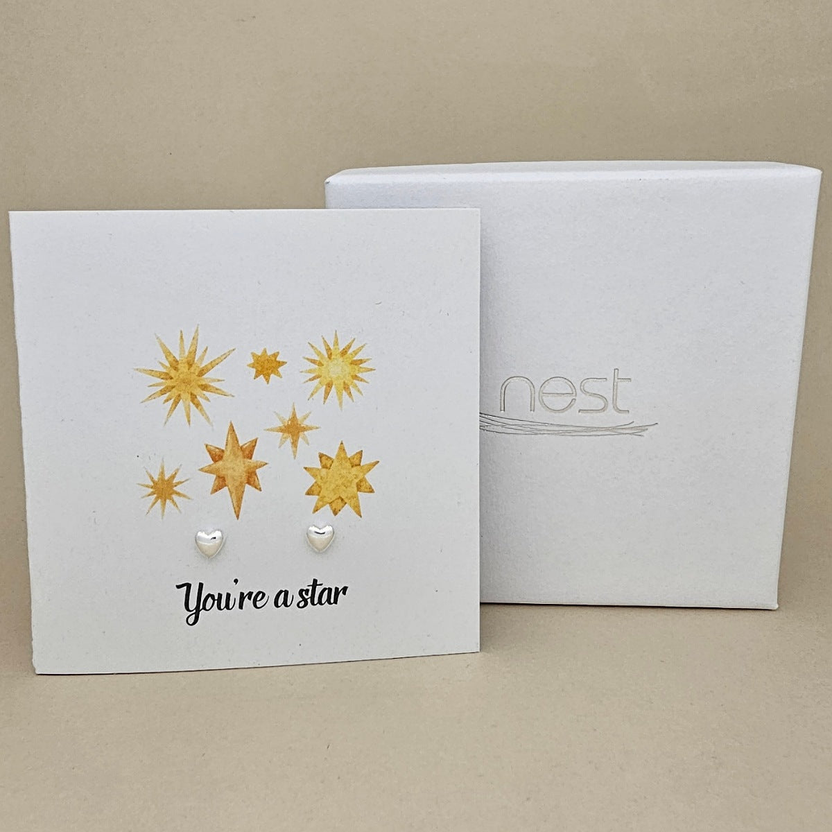 White card with star designs and a pair of silver heart earrings and 'You're a star' text, next to a box labeled 'nest'.