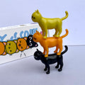 Three cat figurines stacked on top of each other with a colorful box in the background.