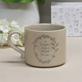 Beige mug with floral wreath design with the wording 'A lucky few have a MUM like you' in the middle on a light surface with flowers and a box in the background
