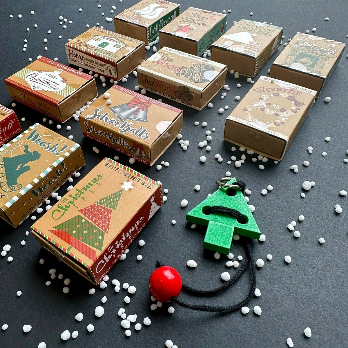 Small cardboard puzzle boxes with Christmas designs on a dark surface with a festive puzzle item showing.