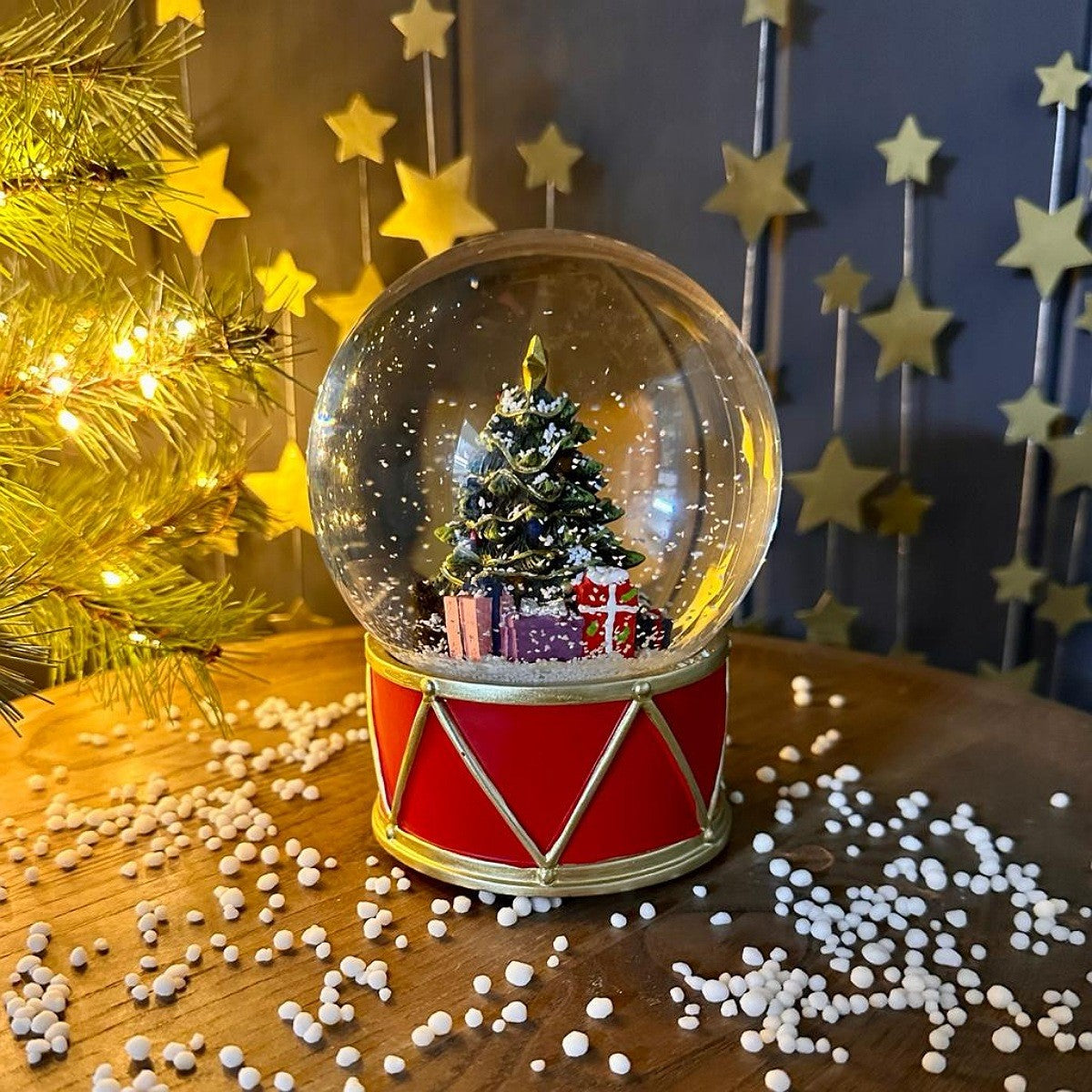 Snow globe with a Christmas tree and presents on a wooden surface with festive decorations.