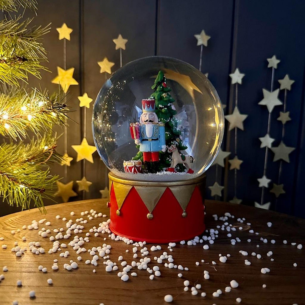 Decorative snow globe with Christmas scene and nutcracker soldier on a wooden surface with festive background