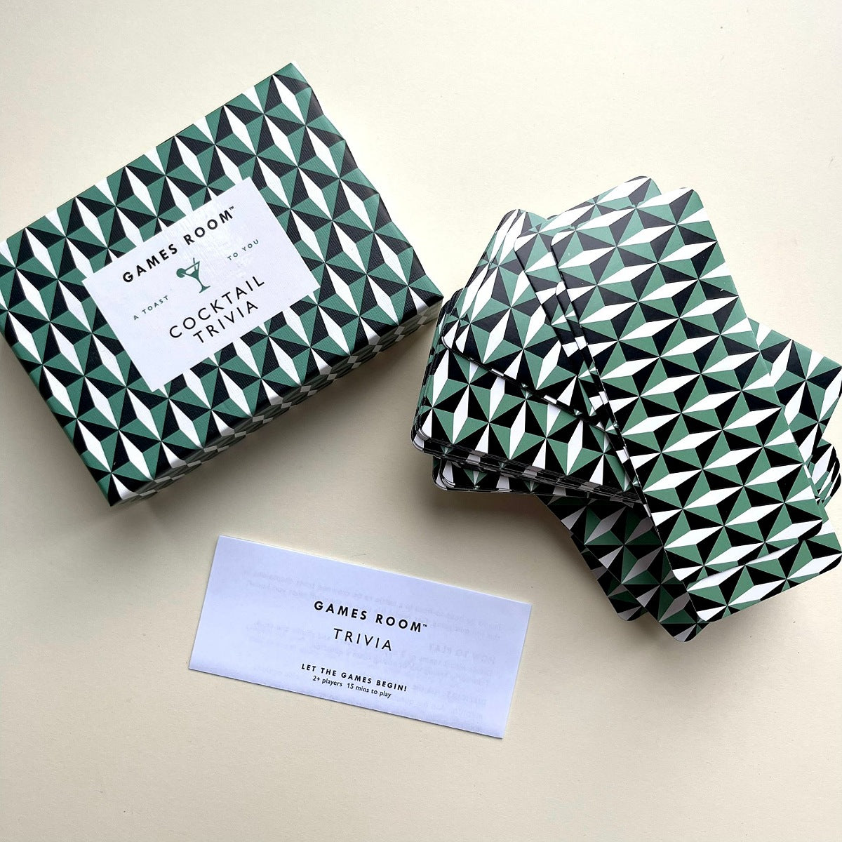 Games Room Cocktail Trivia game box and matching folded cards with a geometric green, black, and white pattern, shown on a light beige background.