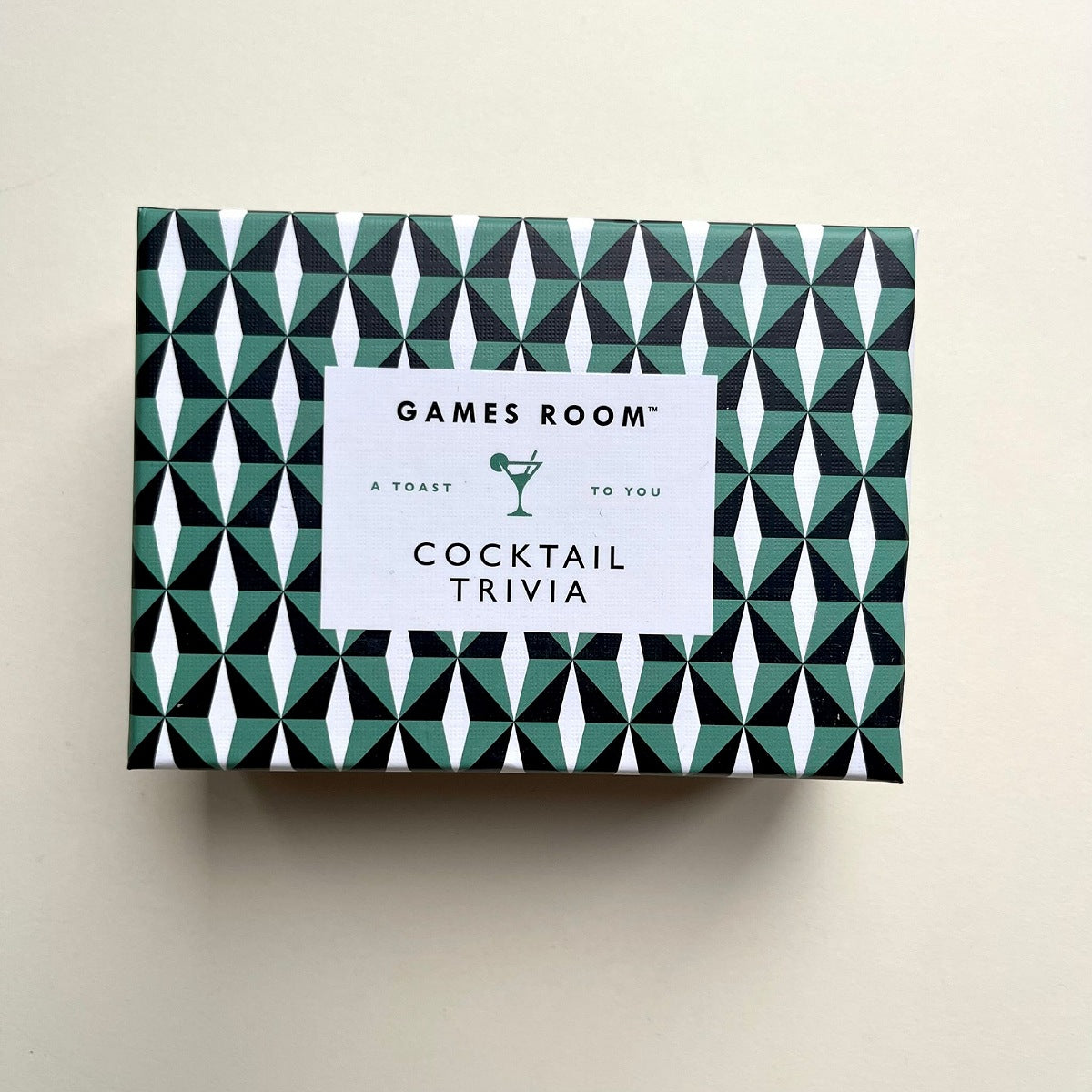 A rectangular box for 'Games Room Cocktail Trivia' featuring a black, white, and green geometric pattern, with a white label in the center.