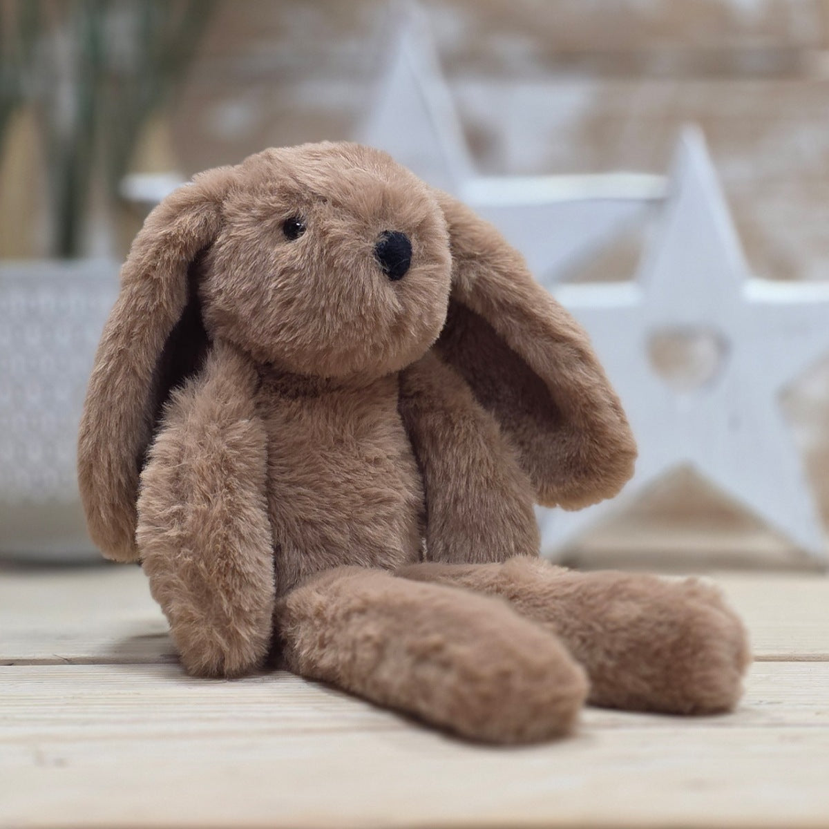 A brown soft fuzzy plush bunny toy, with black eyes and nose, sat on a wooden surface with a blurred star-shaped object in the background
