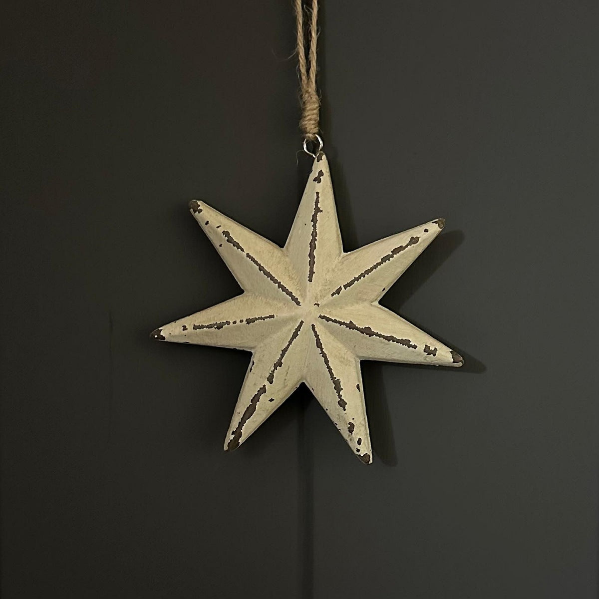 A distressed cream six-pointed star ornament with a rustic dark brown wood-grain pattern, hanging from a natural jute twine string against a dark grey background.