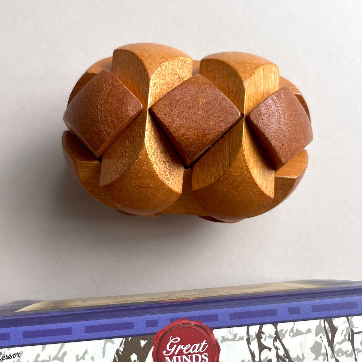 Wooden puzzle ball on a white background with a box labeled 'Great Minds' at the bottom.