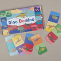 Dino Domino game set with colorful dinosaur-themed cards on a beige background