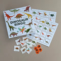 Dinosaur bingo game set with cards, markers, and stickers on a brown background