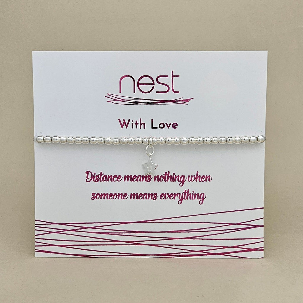 A silver beaded bracelet with a small star charm displayed on a white card from the brand Nest. The card features the text 'With Love' and 'Distance means nothing when someone means everything' in dark pink lettering, set against a neutral beige background.