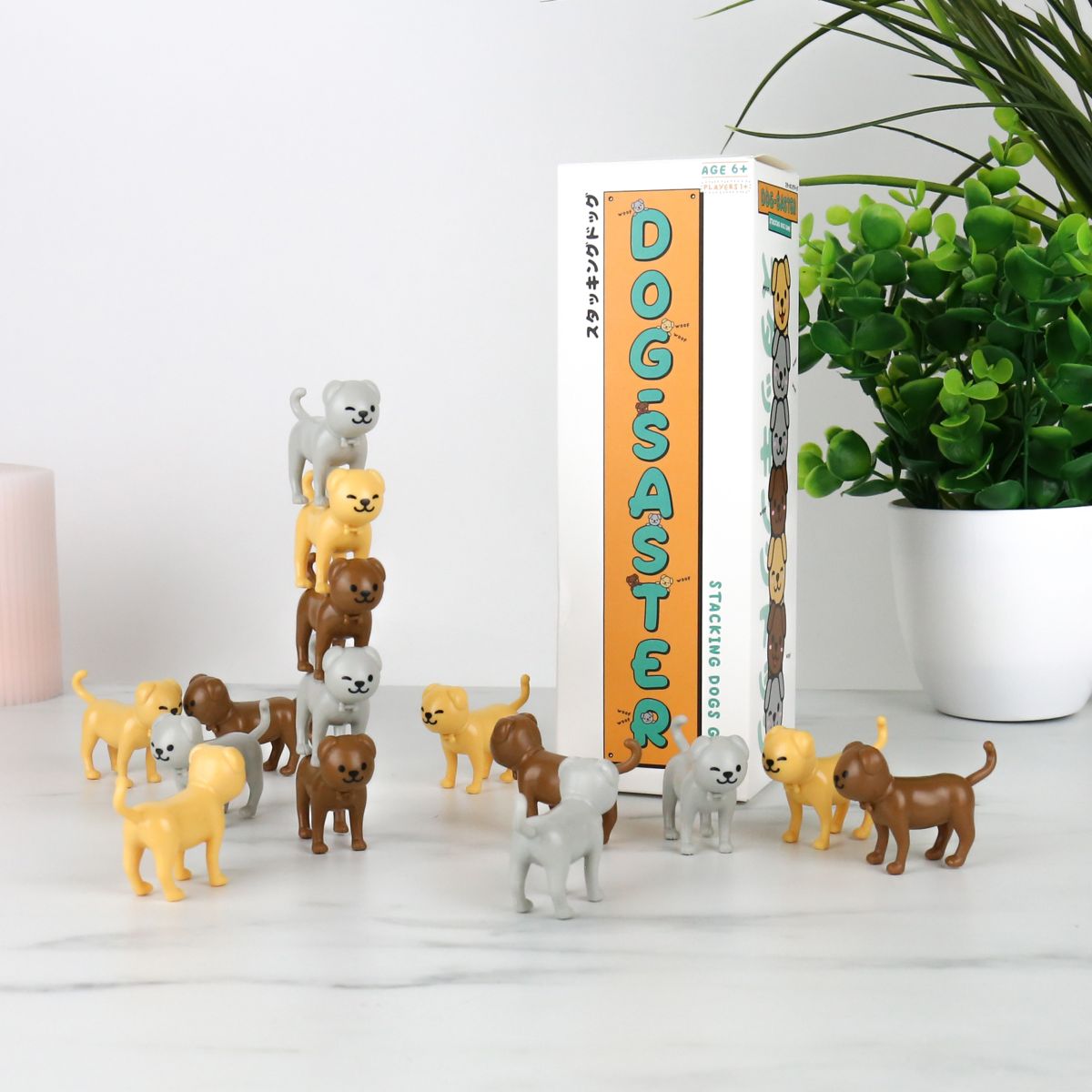 Collection of dog figurines in front of a box labeled 'Dogaster' on a white surface with a plant in the background.