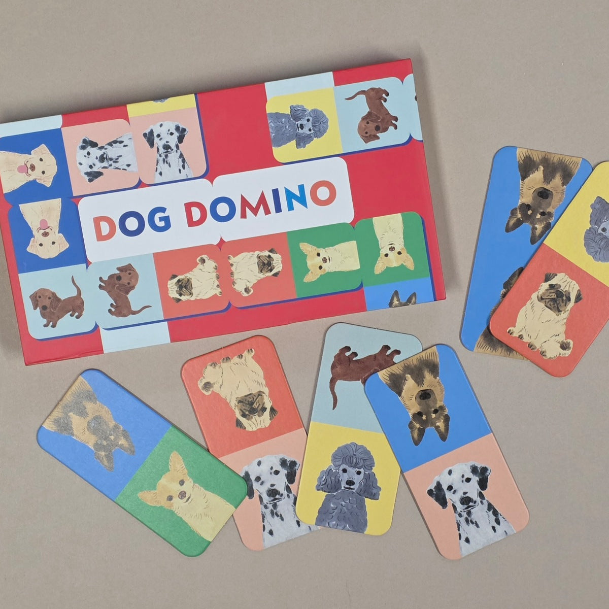 Dog Domino game set with colorful cards featuring dog illustrations on a beige background.