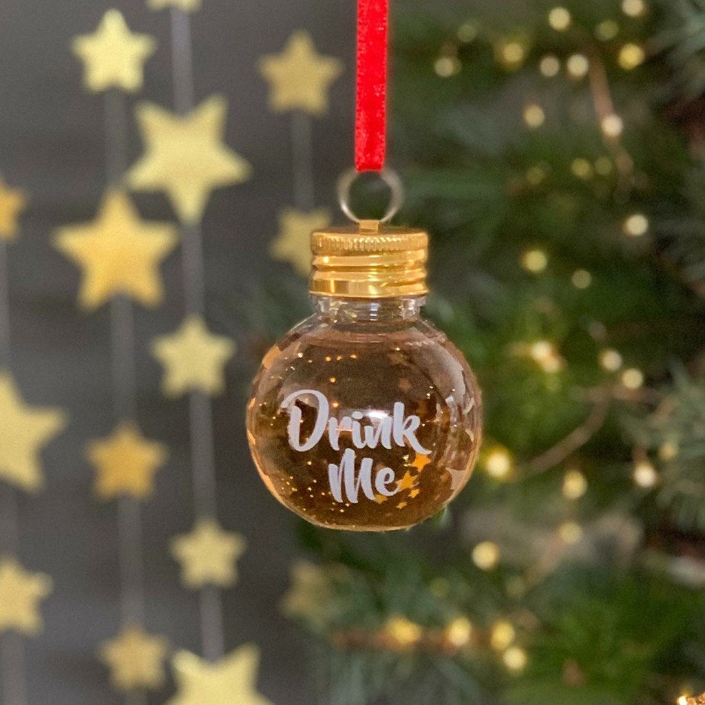 Decorative Christmas plastic ornament with 'Drink Me' text on a gold background, hanging from a red ribbon.