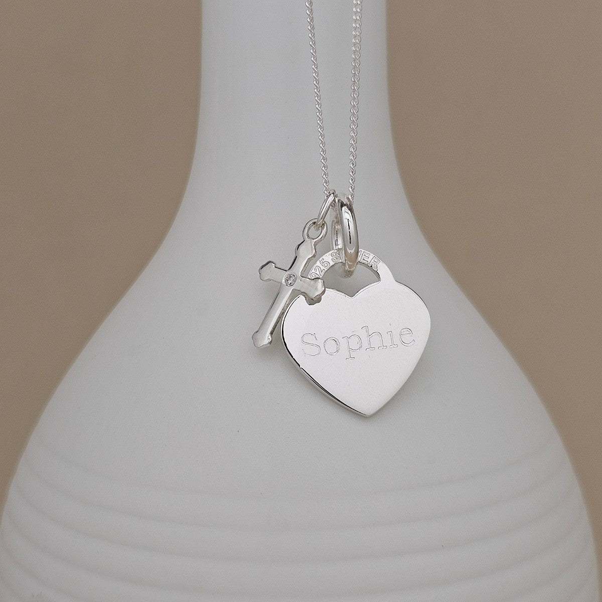 Silver necklace with a heart-shaped pendant engraved with 'Sophie' on a white vase.