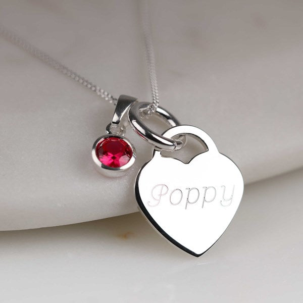 Silver necklace with heart-shaped pendant engraved with 'Poppy' and red gemstone on a light background