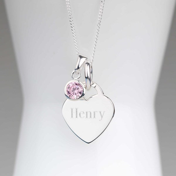 A silver heart-shaped pendant necklace engraved with the name 'Henry', featuring a small round pink gemstone charm on a delicate silver chain, displayed on a white mannequin bust.