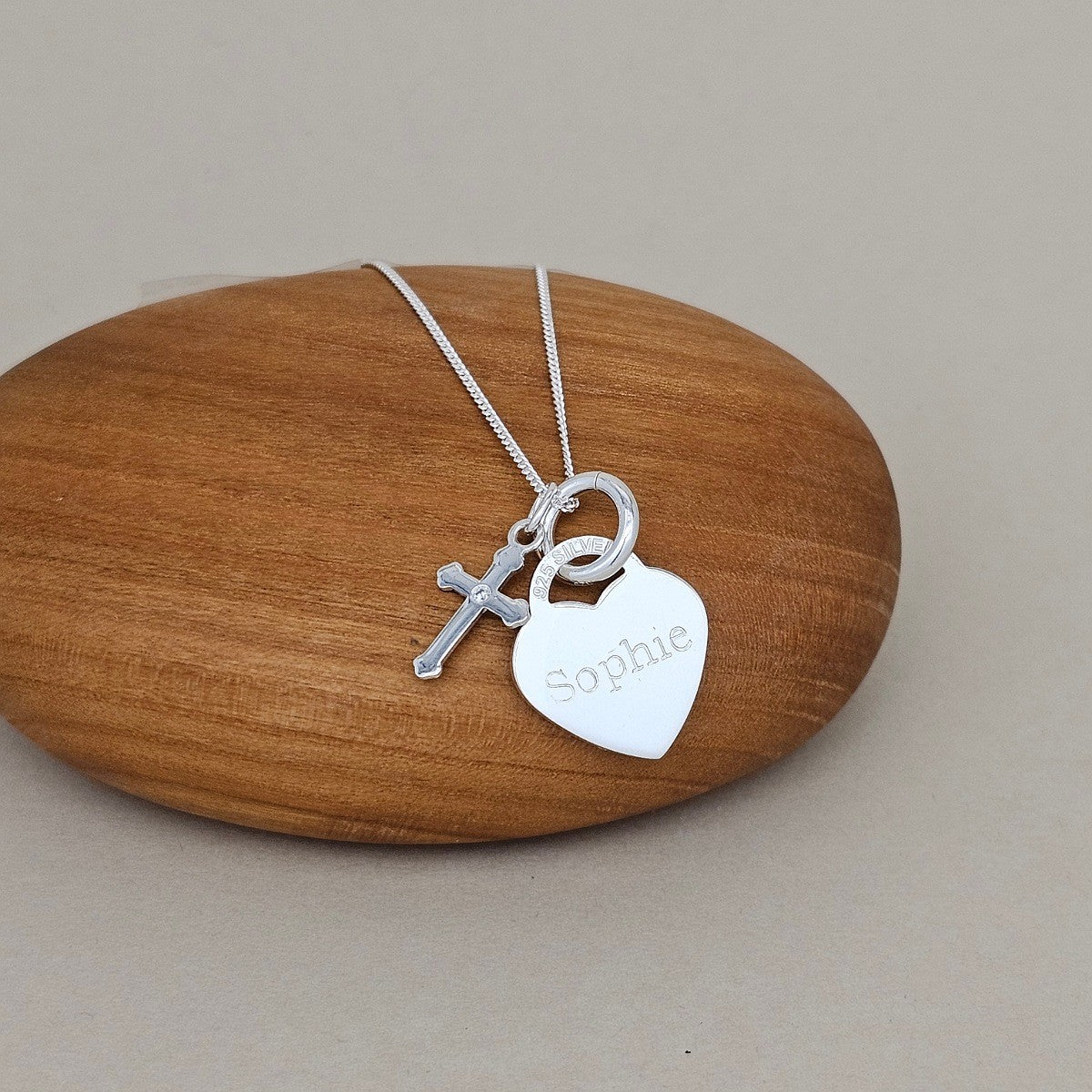 Silver necklace with heart and cross pendant on a wooden surface