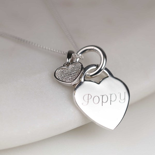 A silver heart pendant necklace with an engraved name and a smaller pavé heart charm.