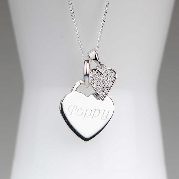 A silver heart pendant necklace with an engraved name and a smaller pavé heart charm, displayed on a white jewelry bust.