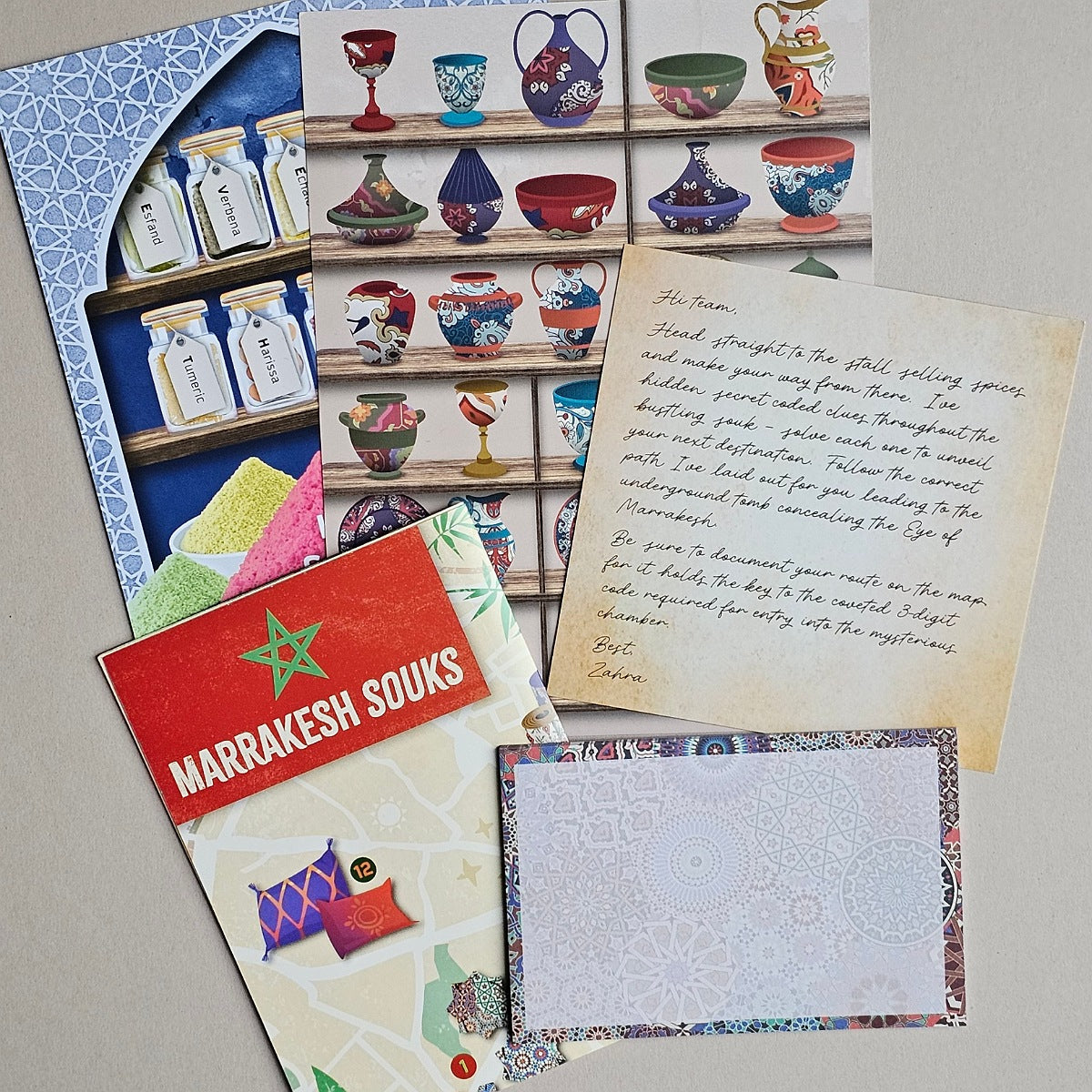 A flat lay of Moroccan-themed stationery and craft paper sheets featuring colorful illustrations of pottery, a red card reading 'MARRAKESH SOUKS,' handwritten notes, and patterned envelopes on a neutral background.