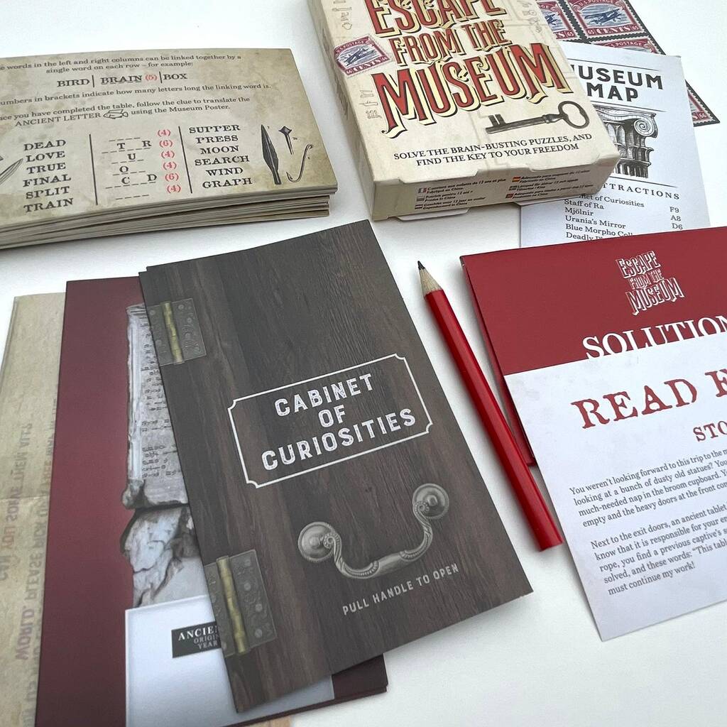 Game components including a book titled 'Cabinet of Curiosities', a pencil, and game instructions on a white surface.