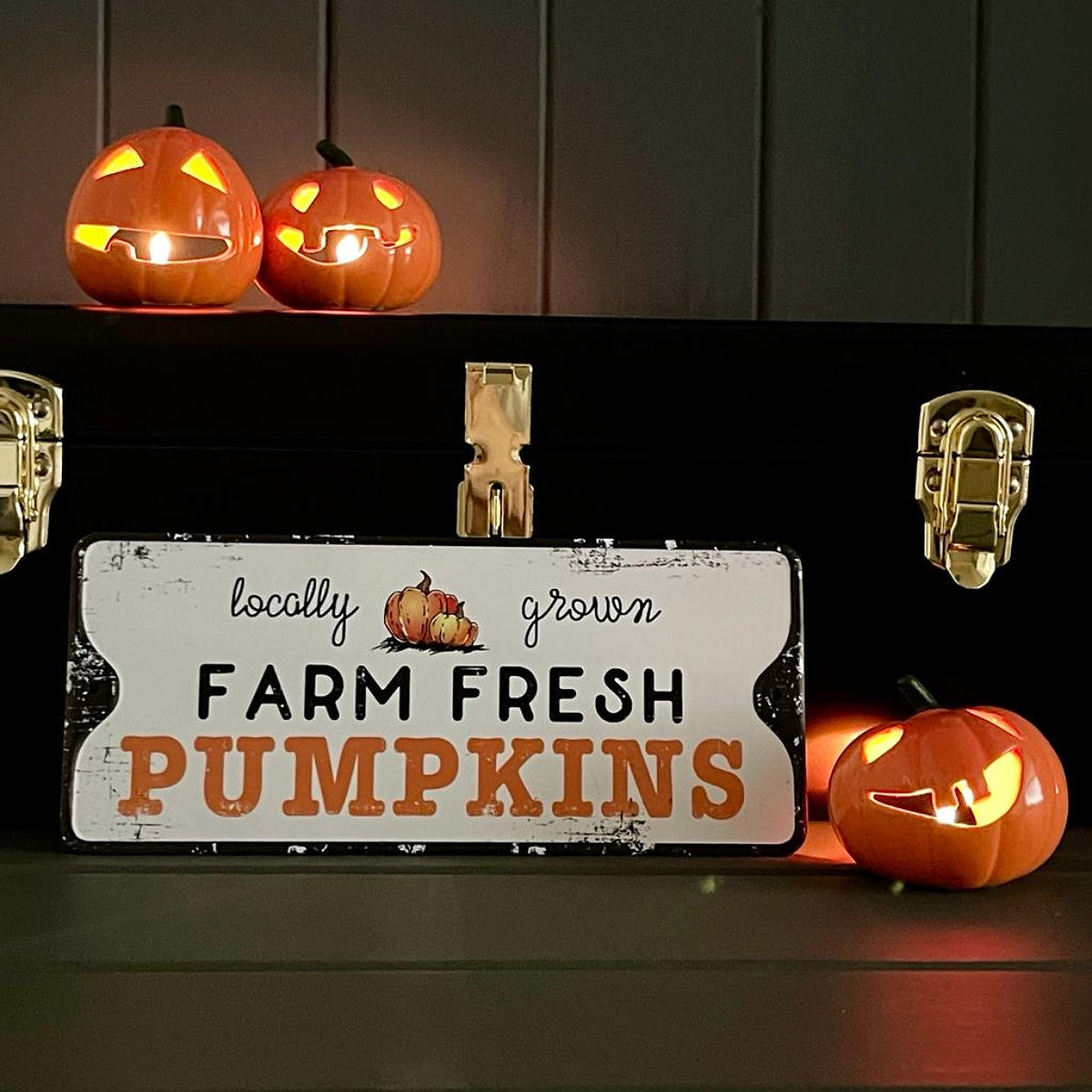 Decorative sign with 'locally grown Farm Fresh Pumpkins' text, surrounded by lit pumpkins on a dark background.