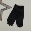 A pair of faux suede black gloves with a fuzzy black pom pom trim at the cuff, displayed on a light beige background next to a decorative wooden star prop
