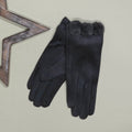 A pair of faux suede grey gloves with a fuzzy grey pom pom trim at the cuff, displayed on a light beige background next to a decorative wooden star prop