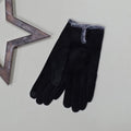 Pair of faux suede black gloves with a thin grey fur trim and three black buttons on a light grey surface with a decorative wooden star frame in the background.