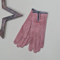 Pair of faux suede dusky pink gloves with a thin grey fur trim and three dusky pink buttons on a light grey surface with a decorative wooden star frame in the background.