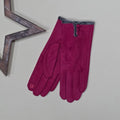Pair of faux suede bright pink gloves with a thin grey fur trim and three bright pink buttons on a light grey surface with a decorative wooden star frame in the background.