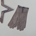 Pair of faux suede mocha gloves with a thin grey fur trim and three mocha buttons on a light grey surface with a decorative metal frame in the background.