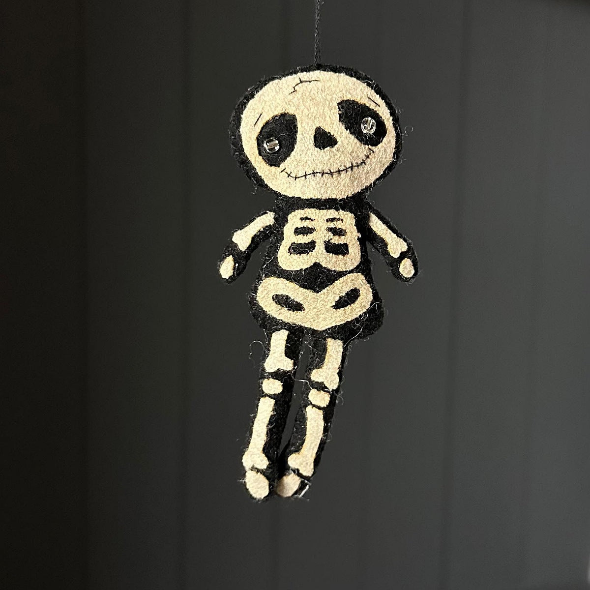 A small felt skeleton hanging ornament against a dark grey background.