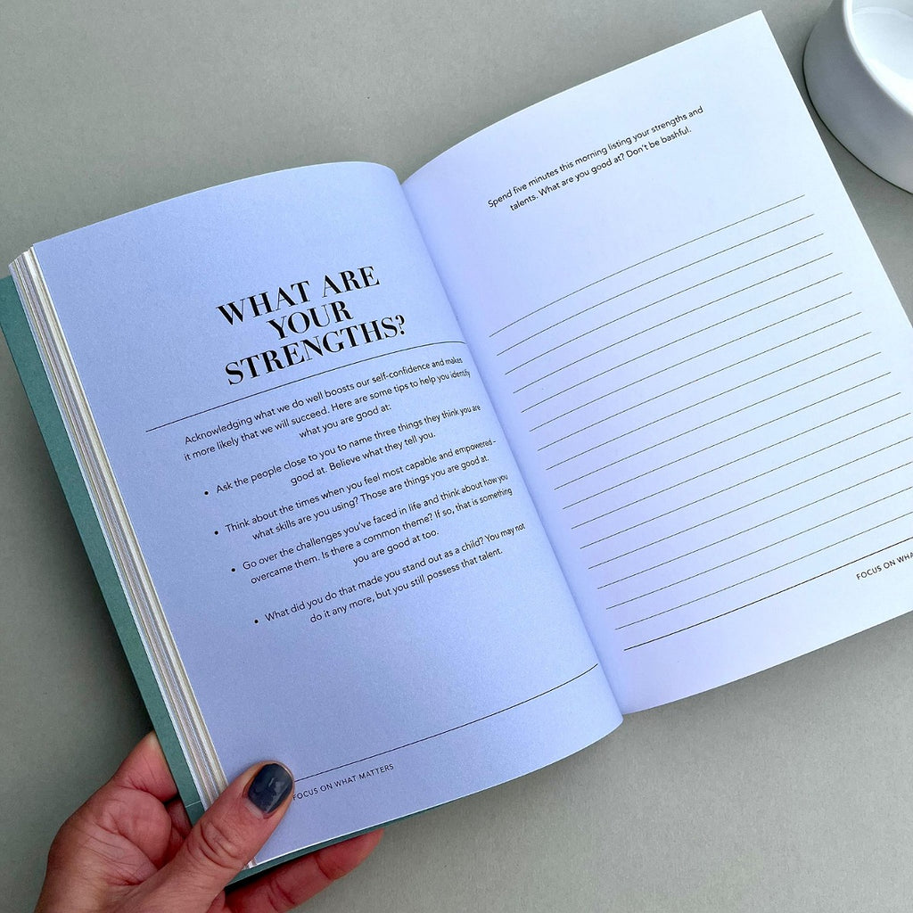 Open book with a question on strengths and lined pages, held by a hand.