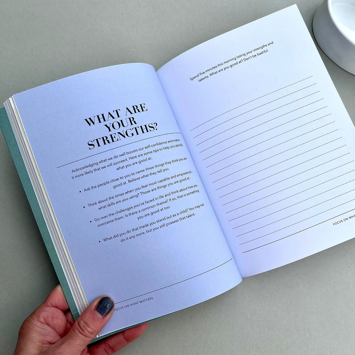 Open book with a question on strengths and lined pages, held by a hand.