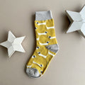 A single yellow sock with a repeating pattern of white sausage dogs with grey ears.  Featuring a light grey cuff, heal and toe, displayed on a neutral beige background with white star-shaped props.
