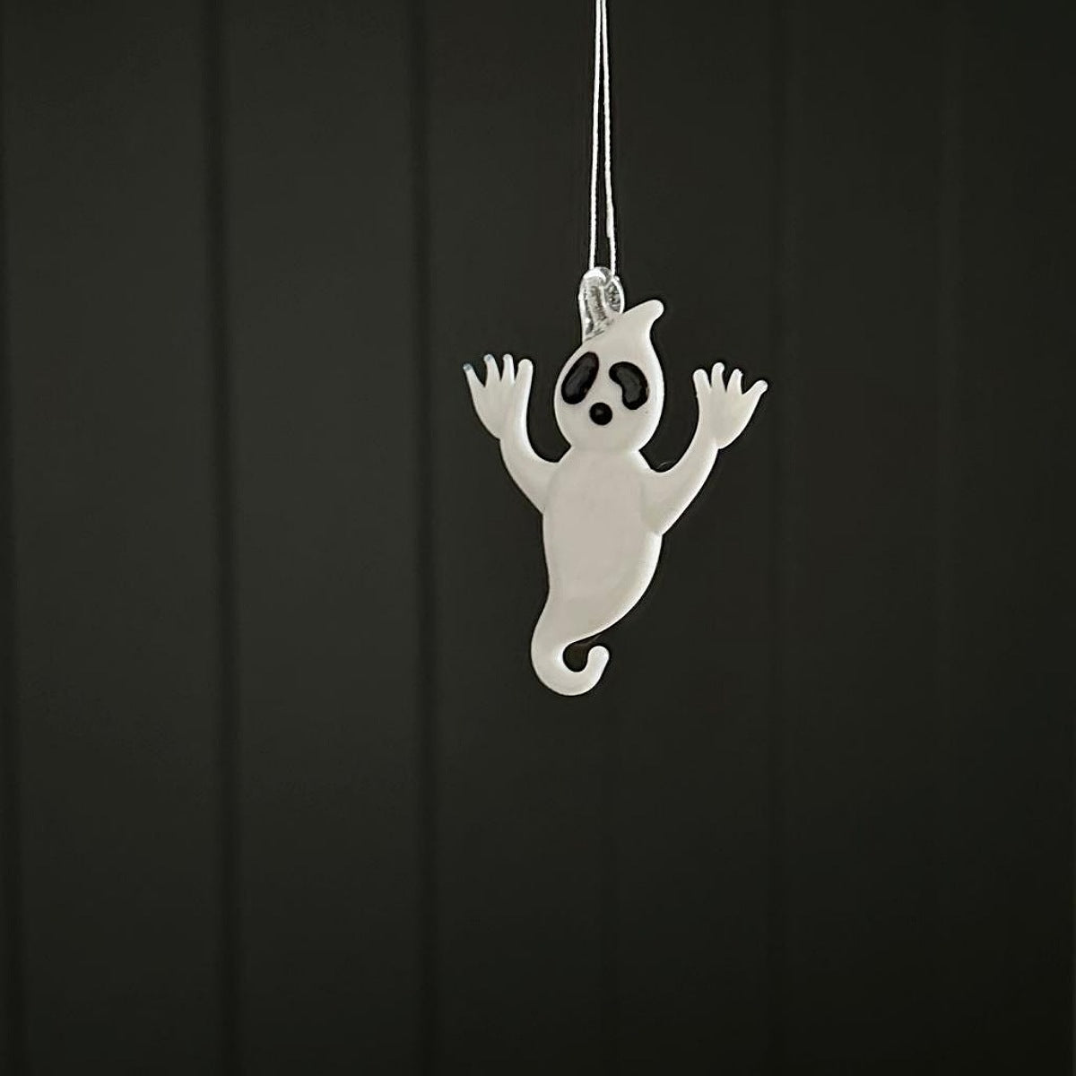 White ghost-shaped ornament hanging against a black background